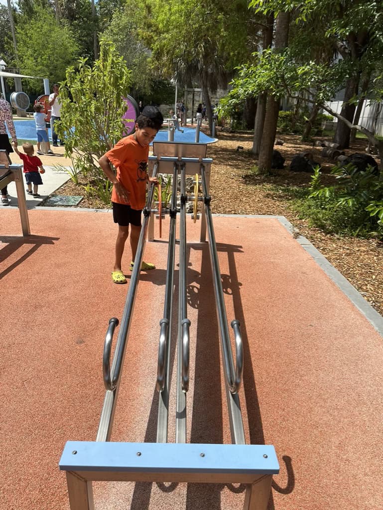 Boy in an orange shirt standing next to a long metal rack. 