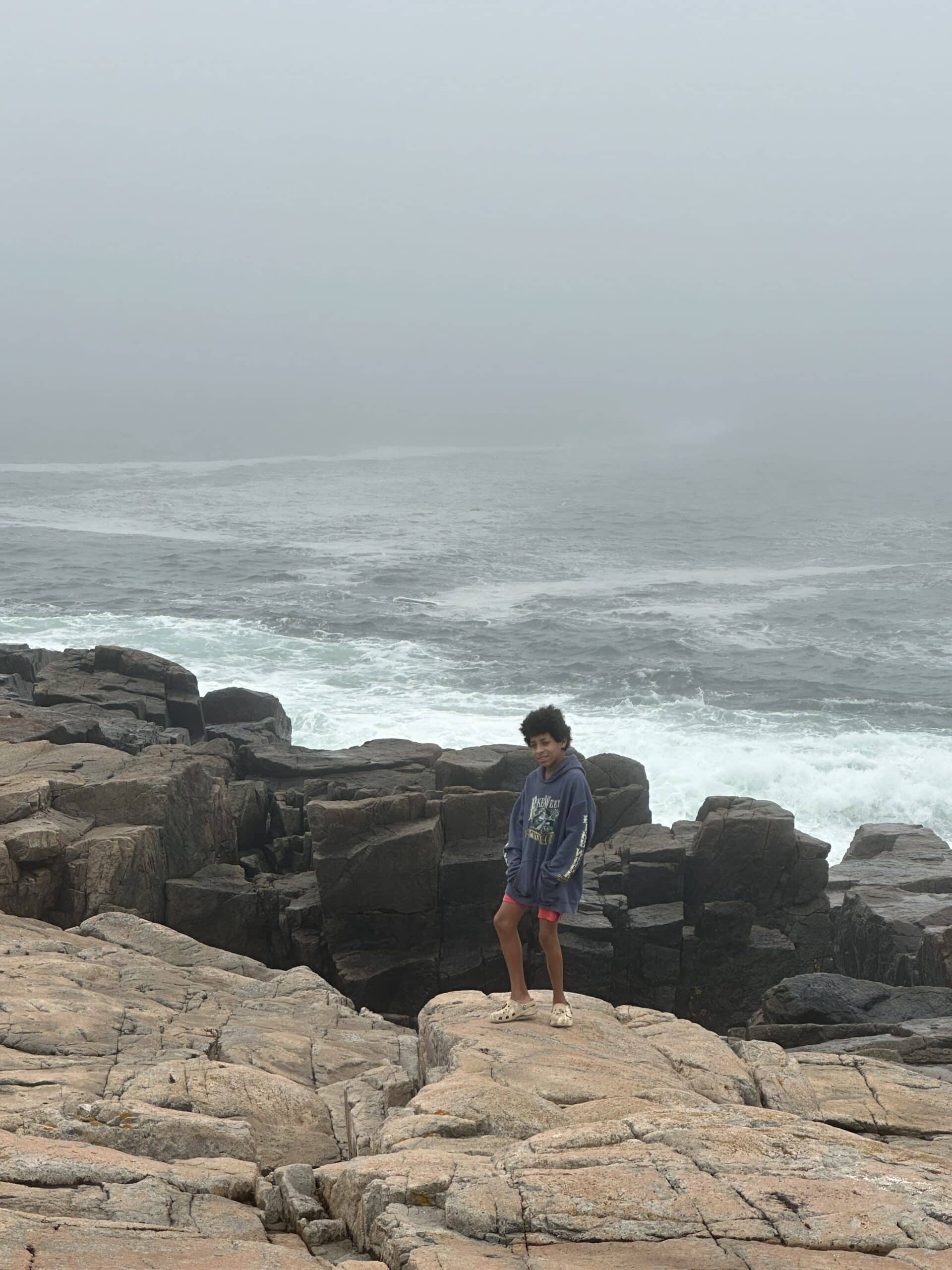 Boy standing on rocks with the water behind him.