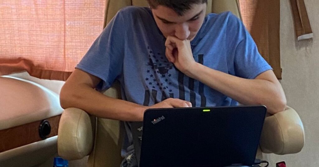 A focused teenager homeschooling inside an RV, intently studying on a laptop, embodying the flexibility and dedication of the homeschool lifestyle on the road.
