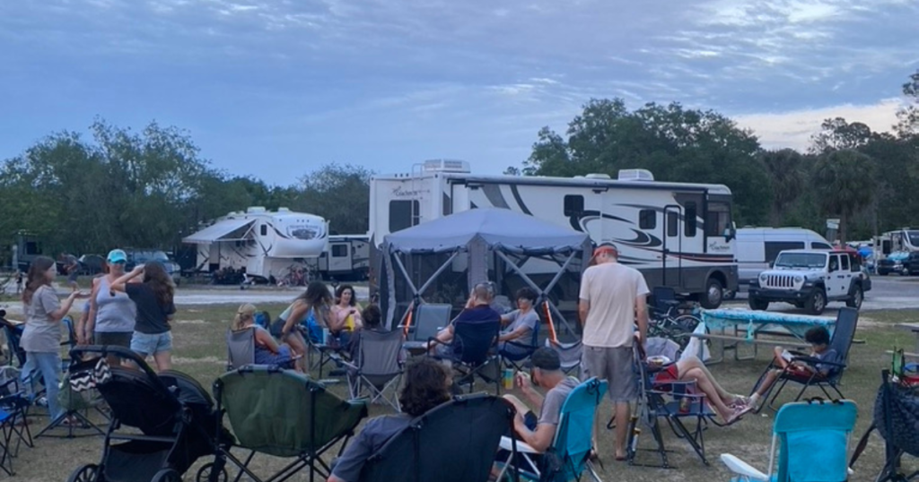 People relax in camping chairs, socializing in the early evening, with various RVs set up in the background, signifying the mobile yet communal way of life embraced by Florida RV residents.