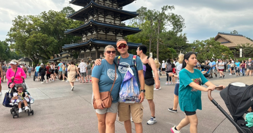 John and I at Epcot in front of the Japanese pagoda. The scene is lively with visitors and families, some with strollers, enjoying their day out.