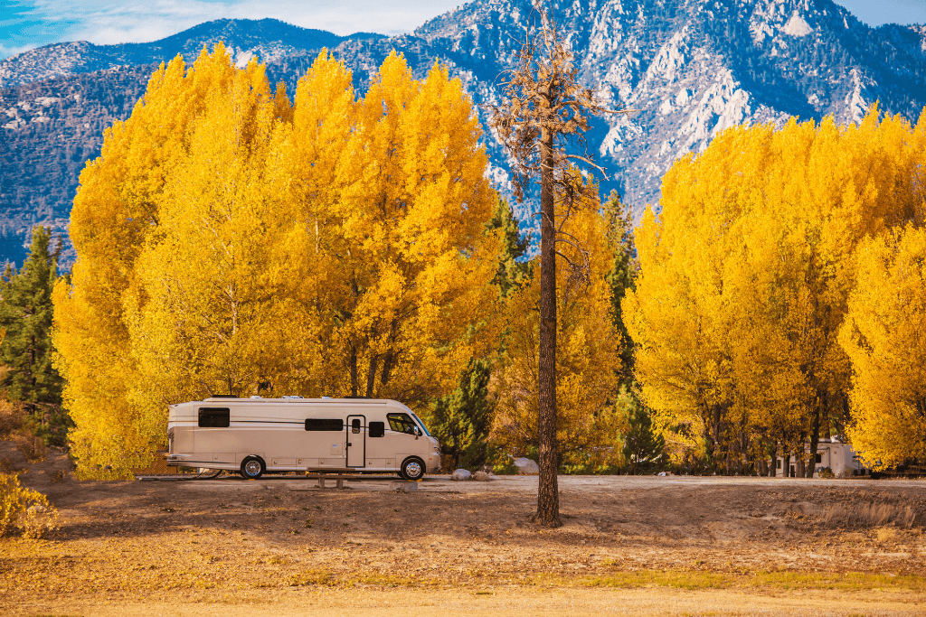 Rv parked with yellow trees and mountains in the back. 