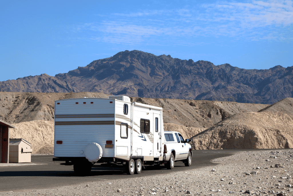 Travel trailer hooked up to a truck on a paved road surrounded by gravel and mountains. 