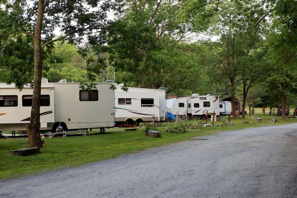 A peaceful RV campground with several RVs parked in a row along a gravel road, highlighting the natural setting and Kentucky RV laws in practice.