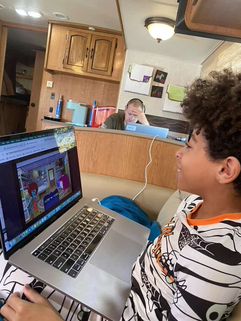 Boy wearing halloween pjs sitting on the couch with a computer. 