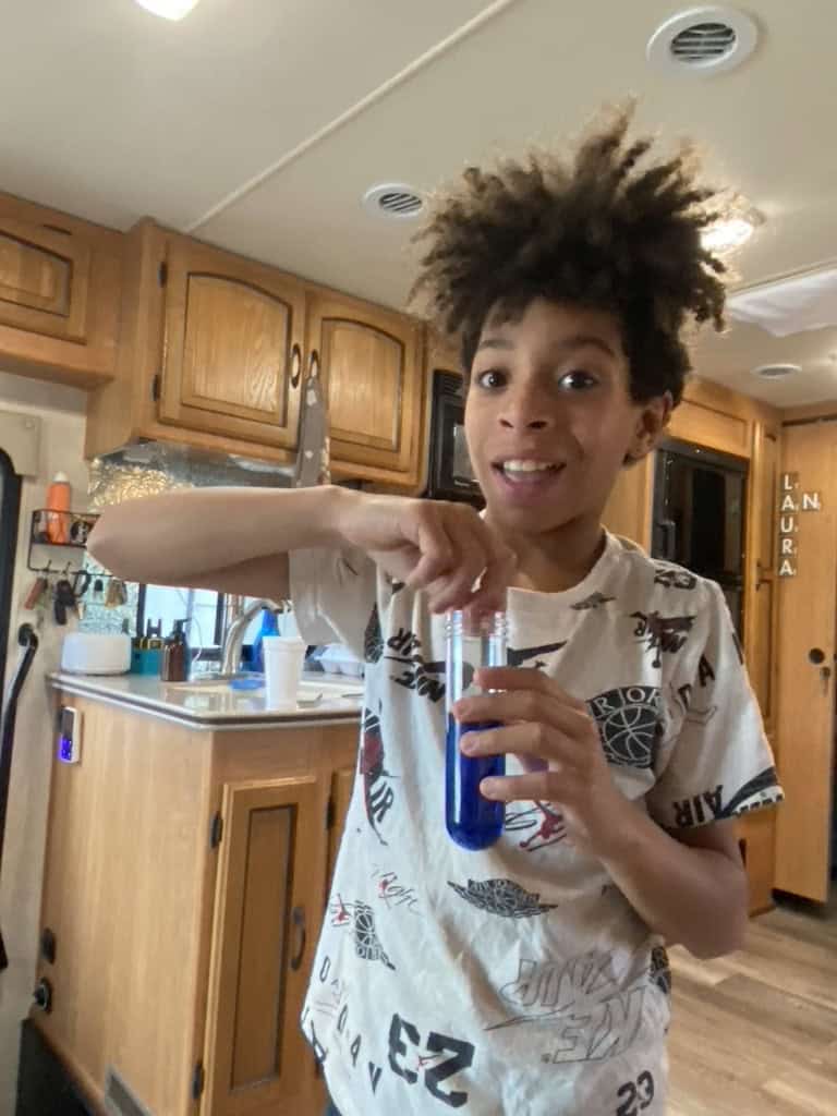 Boy in a white and black shirt holding a test tube filled with blue liquid.