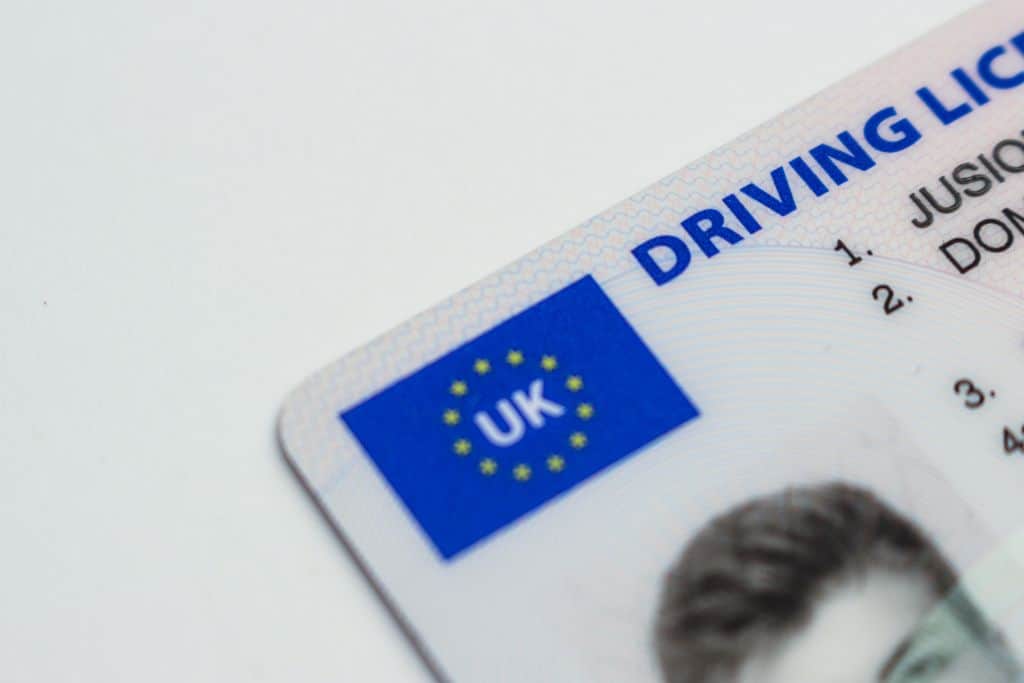This is a close-up of a UK driving license. It prominently features the blue UK flag symbol surrounded by yellow stars, along with the text "DRIVING LICENCE" in bold. Part of the license holder's details and photograph can be seen, though the image focuses primarily on the upper corner and design details.